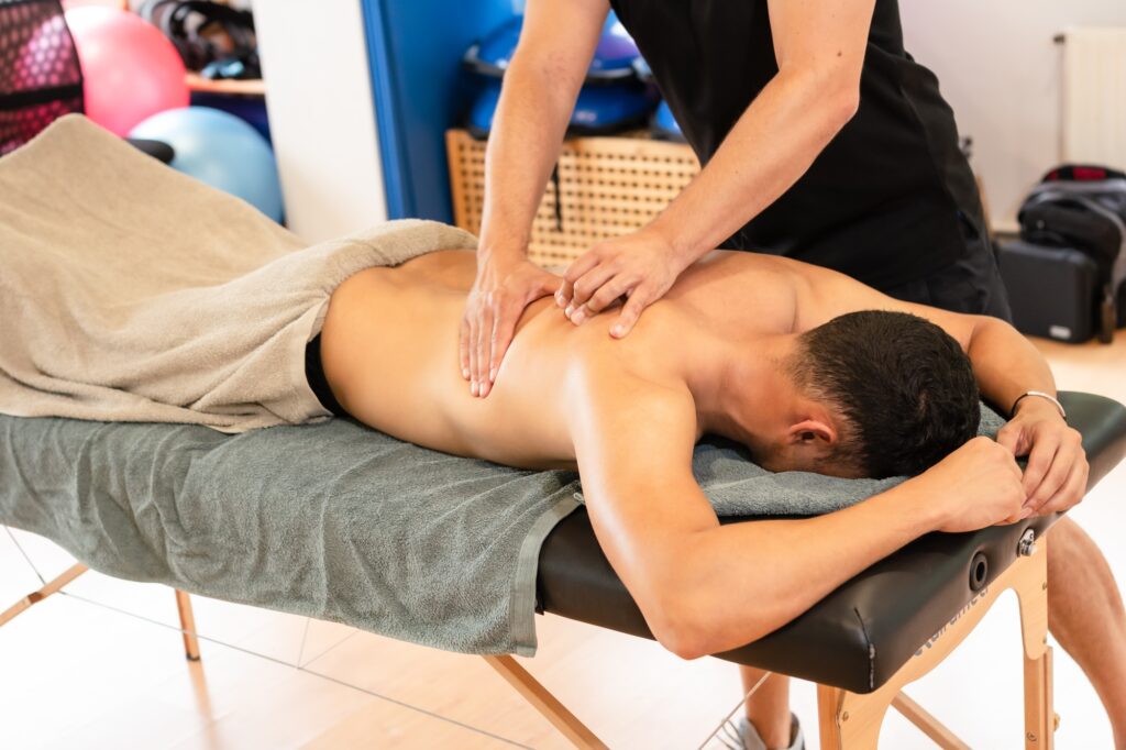 Athletic man receiving a recovery therapeutic back massage by a physiotherapist on a stretcher